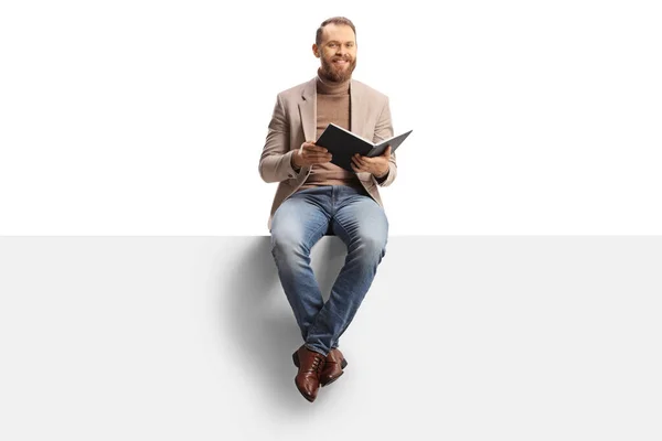 Smiling Young Man Holding Book Sitting Blank Panel Isolated White — Stockfoto