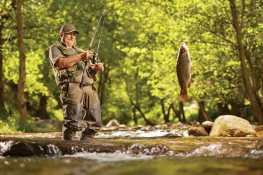 Mature fisherman pulling a carp fish out of a river in the wood