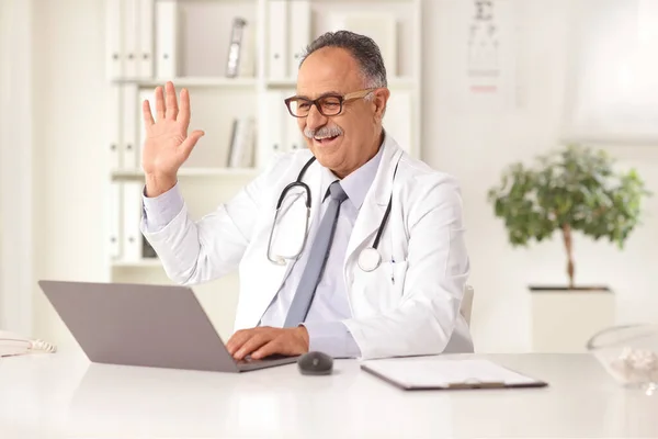 Ältere Männliche Arzt Sitzt Einem Büro Und Winkt Einem Laptop — Stockfoto