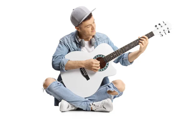 年轻的男性吉他手 坐在地板上弹奏声吉他 背景是白色的 — 图库照片