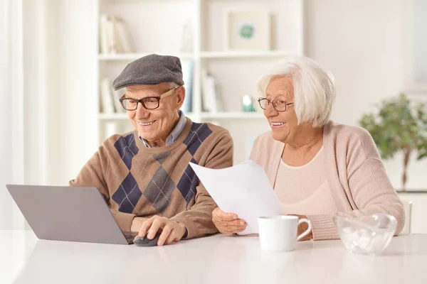 幸せな高齢者の男性と女性の文書を保持し 自宅でノートパソコンを見て — ストック写真