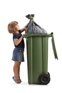 Küçük bir kızın beyaz arka planda izole edilmiş plastik bir kutuya atık poşeti koyarken tam boy profil fotoğrafı.