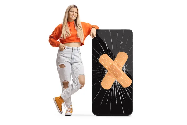 女青少年靠在一个大手机上 手机上有破碎的屏幕和白色背景隔离的粘贴绷带 — 图库照片