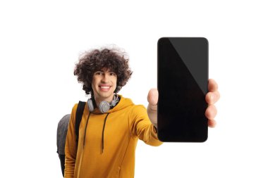 Kıvırcık saçlı, akıllı telefon gösteren ve beyaz arka planda izole edilmiş kameraya gülümseyen bir erkek öğrenci.