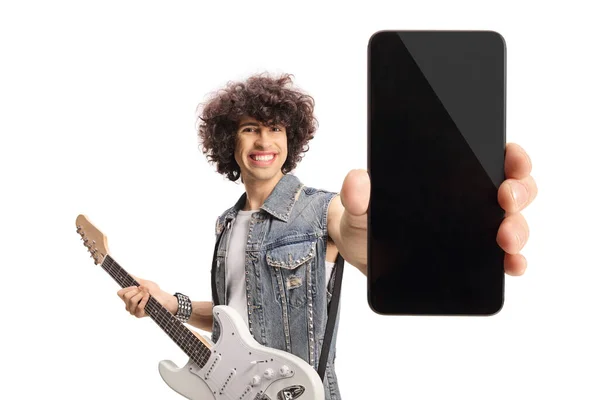 白を基調としたスマートフォンを見せるエレキギター付きデニムベストの若い男 — ストック写真