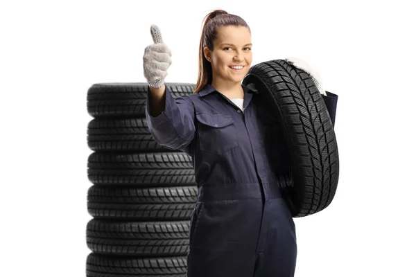 若い女性整備士の労働者が車のタイヤを持っていると白の背景に隔離された親指を表示 — ストック写真