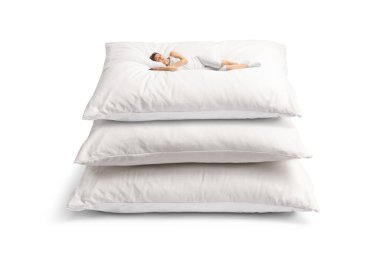 Beyaz pijamalı genç bir kadın beyaz arka planda izole edilmiş büyük yastıkların üzerinde uyuyor.