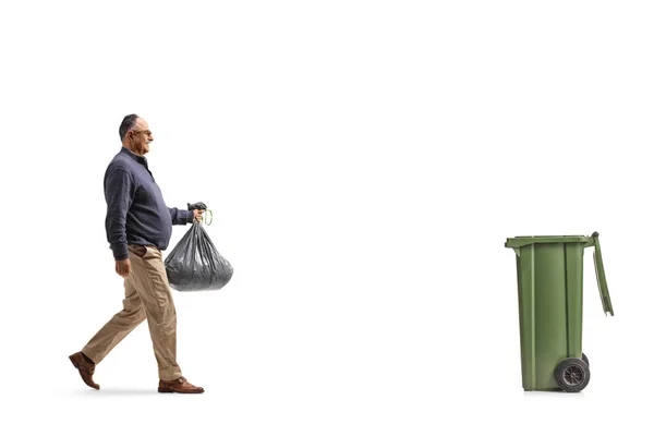 白い背景に隔離されたゴミ箱に向かって歩いているのがプラスチック製のゴミ袋を持っている成熟した男の完全な長さのプロフィール — ストック写真