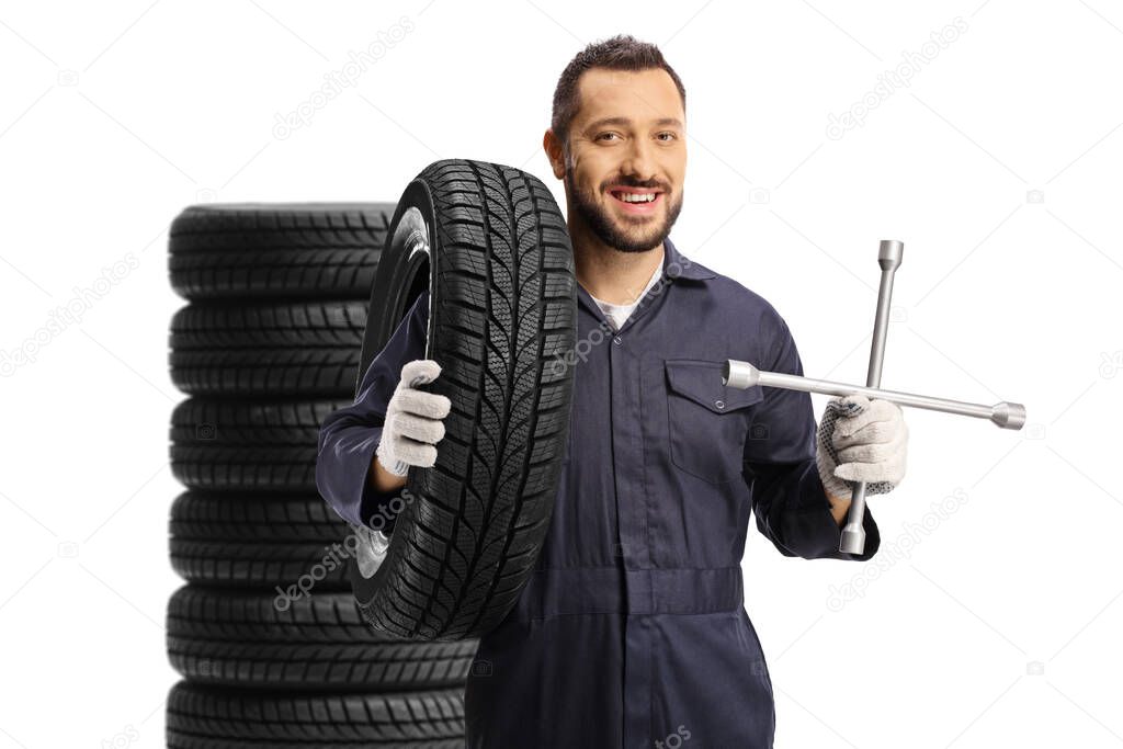 Auto mechanic standing in front of tires and holding a lug wrench isolated on white background