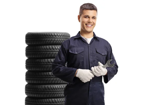 年轻的机械工人拿着扳手微笑 站在用白色衬底隔开的轮胎前 — 图库照片