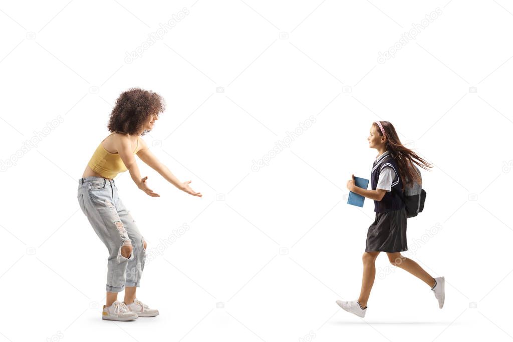 Full length profile shot of a schoolgirl with a book running towards a young woman isolated on white background