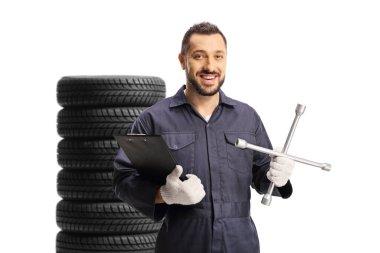 Otomobil tamircisi beyaz arka planda izole edilmiş lastik yığınının önünde bir pano ve bijon anahtarı tutuyor.