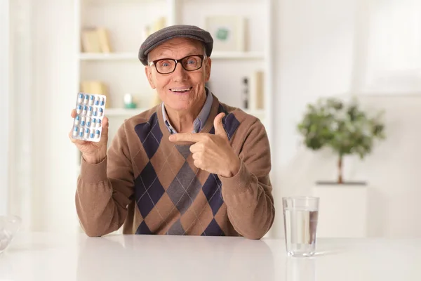 Smiling Elderly Man Sitting Home Pointing Pack Pills — Foto Stock