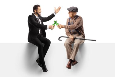 Yaşlı bir adam ve bir iş adamı boş bir panelde oturup beyaz arka planda izole edilmiş birayla kadeh kaldırıyorlar.