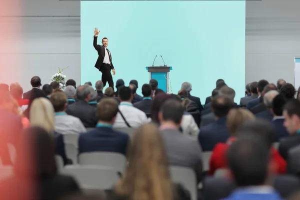 Businessman waving on stage and people watching in the audience at a conference