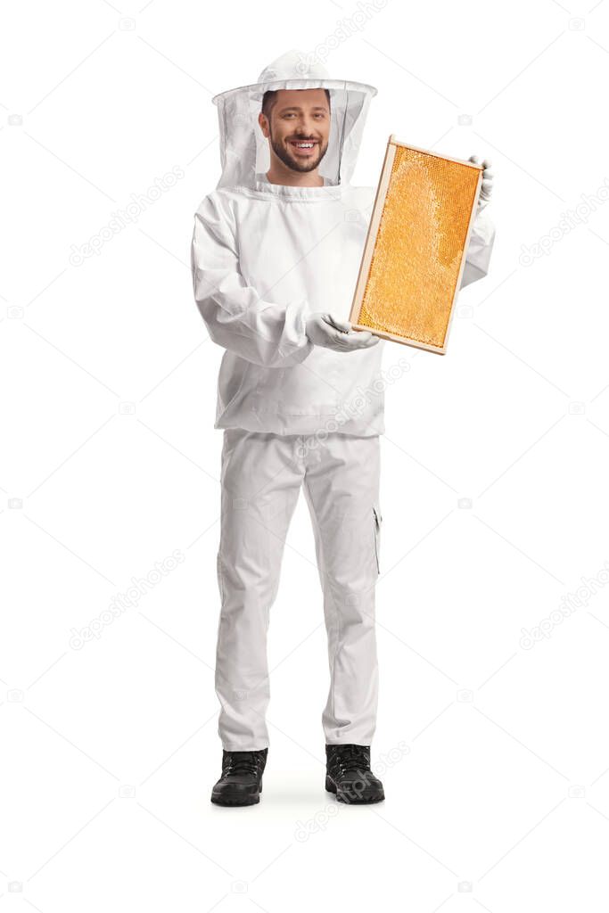 Young male bee keeper in a uniform holding a honeycomb frame isolated on white background