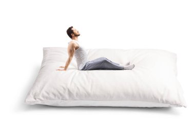 Beyaz arka planda izole edilmiş büyük bir yastığa uzanan pijamalı genç adam.