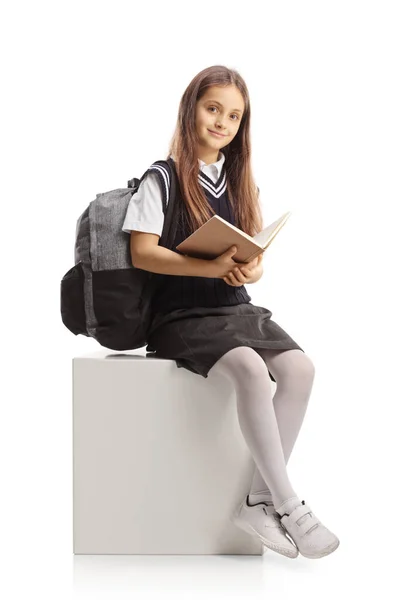 Schoolgirl Sitting White Cube Reading Book Isolated White Background — Zdjęcie stockowe