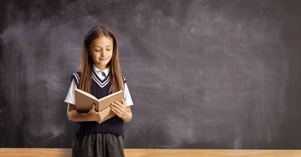 Schoolgirl Reading Book Front Blackboard — Zdjęcie stockowe