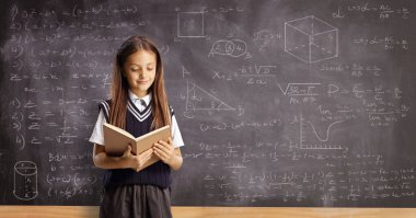Pupil reading a book and standing in front of a blackboard with geometry and math formulas