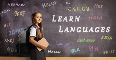 Schoolgirl with a backpack and book in front of a language school blackboard 