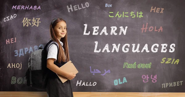 Schoolgirl with a backpack and book in front of a language school blackboard