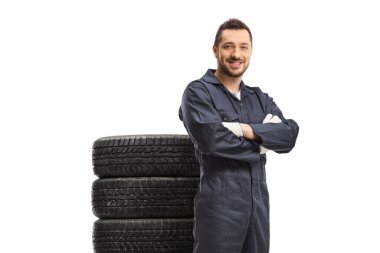 Smiling car mechanic posing with a pile of tires behind him isolated on white background