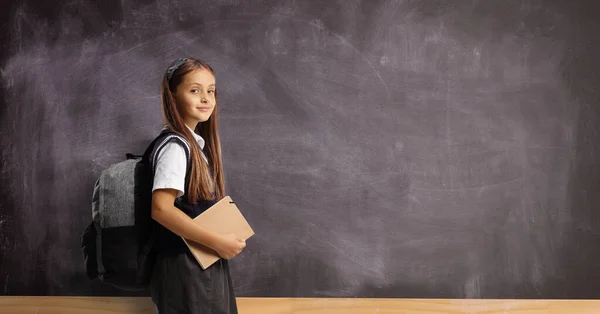 Schoolgirl Backpack Book Standing Front Blank Blackboard Looking Camera — Zdjęcie stockowe