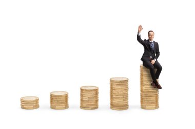 Businessman sitting on a pile of coins and waving at camera isolated on white background
