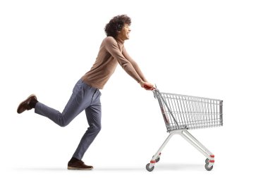 Full length profile shot of a young man running with an empty shopping cart isolated on  white background