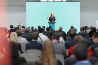 Woman giving a speech on a podium and people sitting in the audience at a business conference