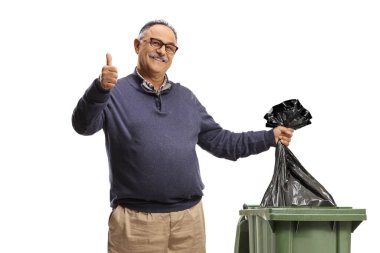Olgun bir adam çöp kutusuna plastik bir torba atıyor ve beyaz arka planda izole edilmiş bir işaret veriyor.