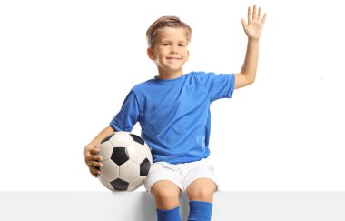 Beyaz arka planda izole edilmiş bir futbol topuyla boş bir panele el sallayan ve oturan çocuk.