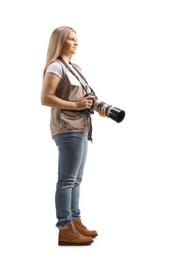 Beyaz arka planda izole edilmiş bir kamera taşıyan genç bir kadın fotoğrafçının tam boy profil fotoğrafı.