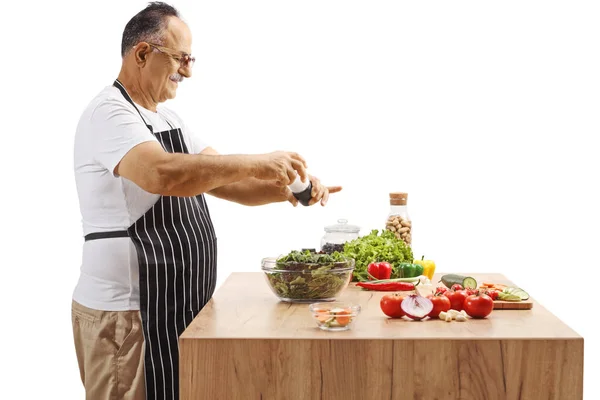 白い背景に隔離されたキッチンカウンターでサラダを味付け成熟した男のサイドショット — ストック写真