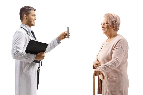 Młody Lekarz Pokazuje Telefon Komórkowy Starszej Kobiecie Odizolowanej Białym Tle — Zdjęcie stockowe