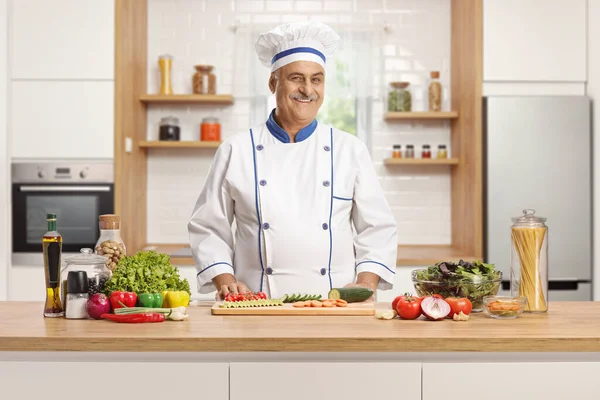 微笑着成熟的男性厨师 摆出一副在厨房里摆设蔬菜柜台的姿势 — 图库照片