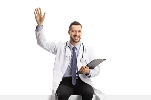 Young Male Doctor Sitting Blank Panel Waving Isolated White Background — Stock Photo, Image