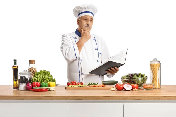 穿着制服的成熟的男厨师拿着一本烹饪书 思考着如何在白色背景下独立做饭 — 图库照片