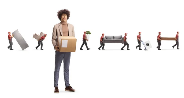一个年轻优雅的男人拿着纸盒和搬运工的全长肖像画 这些搬运工带着家居用品和家具 背景是白色的 — 图库照片