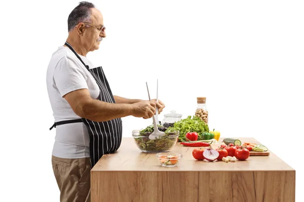 白い背景に隔離された新鮮なサラダを準備する木製のカウンターの後ろに成熟した男のサイドショット — ストック写真