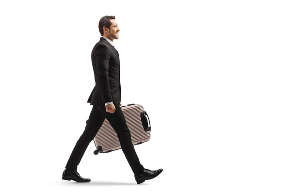 白い背景に隔離されたスーツケースと一緒に歩くビジネスマンの完全な長さのプロフィールショット — ストック写真