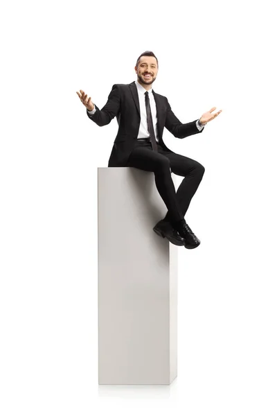 陽気なビジネスマンは背の高い白い柱の上に座って 白い背景に隔離されたカメラで笑顔 — ストック写真