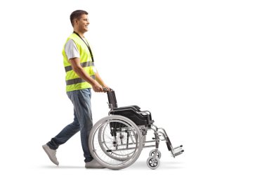 Beyaz arka planda izole edilmiş boş bir tekerlekli sandalyeyi iten bir erkek toplum çalışanının tam boy profil çekimi.