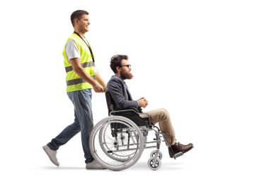 Tekerlekli sandalyedeki bir adamı beyaz arka planda iten bir kamu çalışanının uzun metrajlı fotoğrafı.