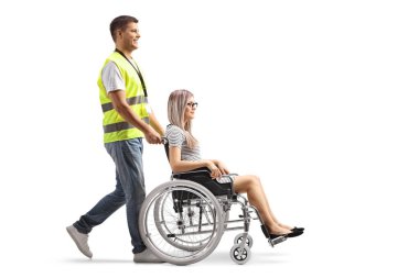 Bir kamu çalışanının beyaz arka planda izole edilmiş tekerlekli sandalyedeki genç bir kadını iterken tam boy profil çekimi.