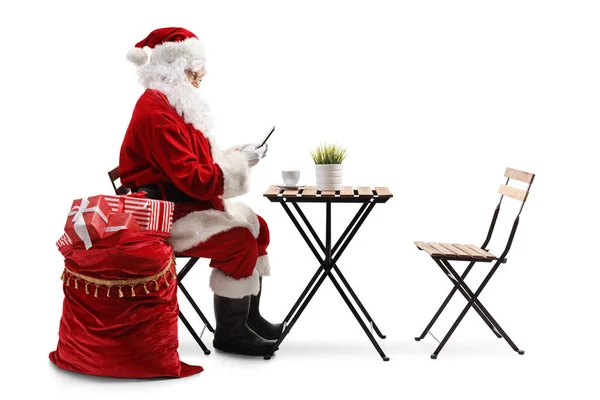 Santa Claus Siedzi Przy Stoliku Kawiarni Używa Smartfona Odizolowanego Białym — Zdjęcie stockowe