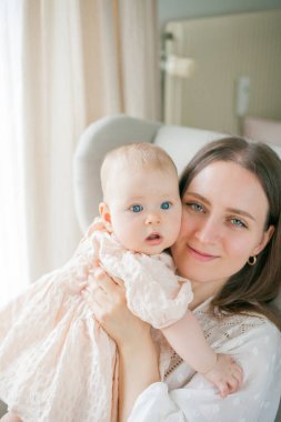 Mutlu genç anne, beş aylıkken kızını kucağında tutuyor. Evdeki bir sandalyede oturuyor..
