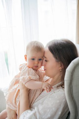 Mutlu genç anne, beş aylıkken kızını kucağında tutuyor. Evdeki bir sandalyede oturuyor..