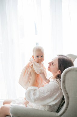 Mutlu genç anne, beş aylıkken kızını kucağında tutuyor. Evdeki bir sandalyede oturuyor..
